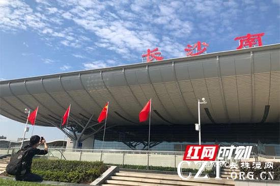 一位旅客正在国旗下以“长沙南”三个字为背景,拍照留念。